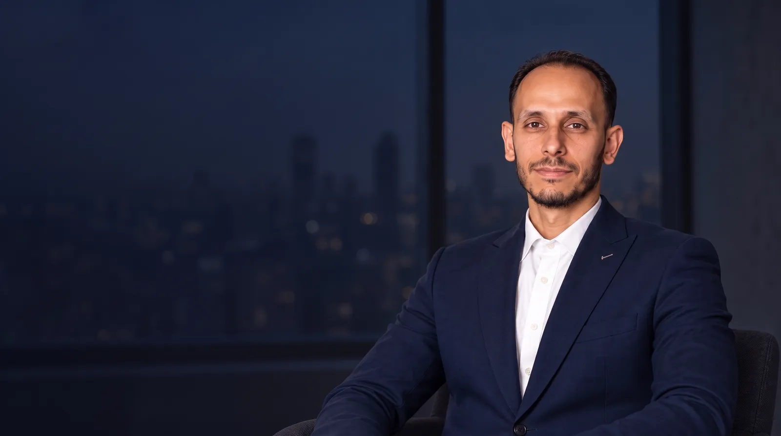 Saed Hassunah in the approved session, against a dark sky-blue background without trees, with subtle red lighting and calm space for text